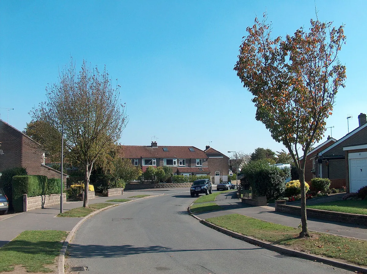 Brick semi-detached houses and bungalows with front lawns along a curving estate road in Dronfield Woodhouse