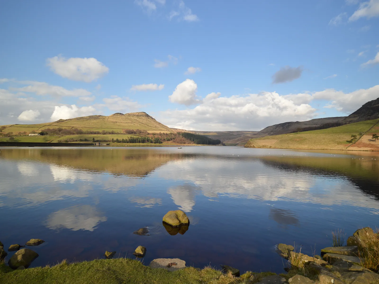 Dovestone Reservoir reflecting blue sky and clouds, with moorland hills behind