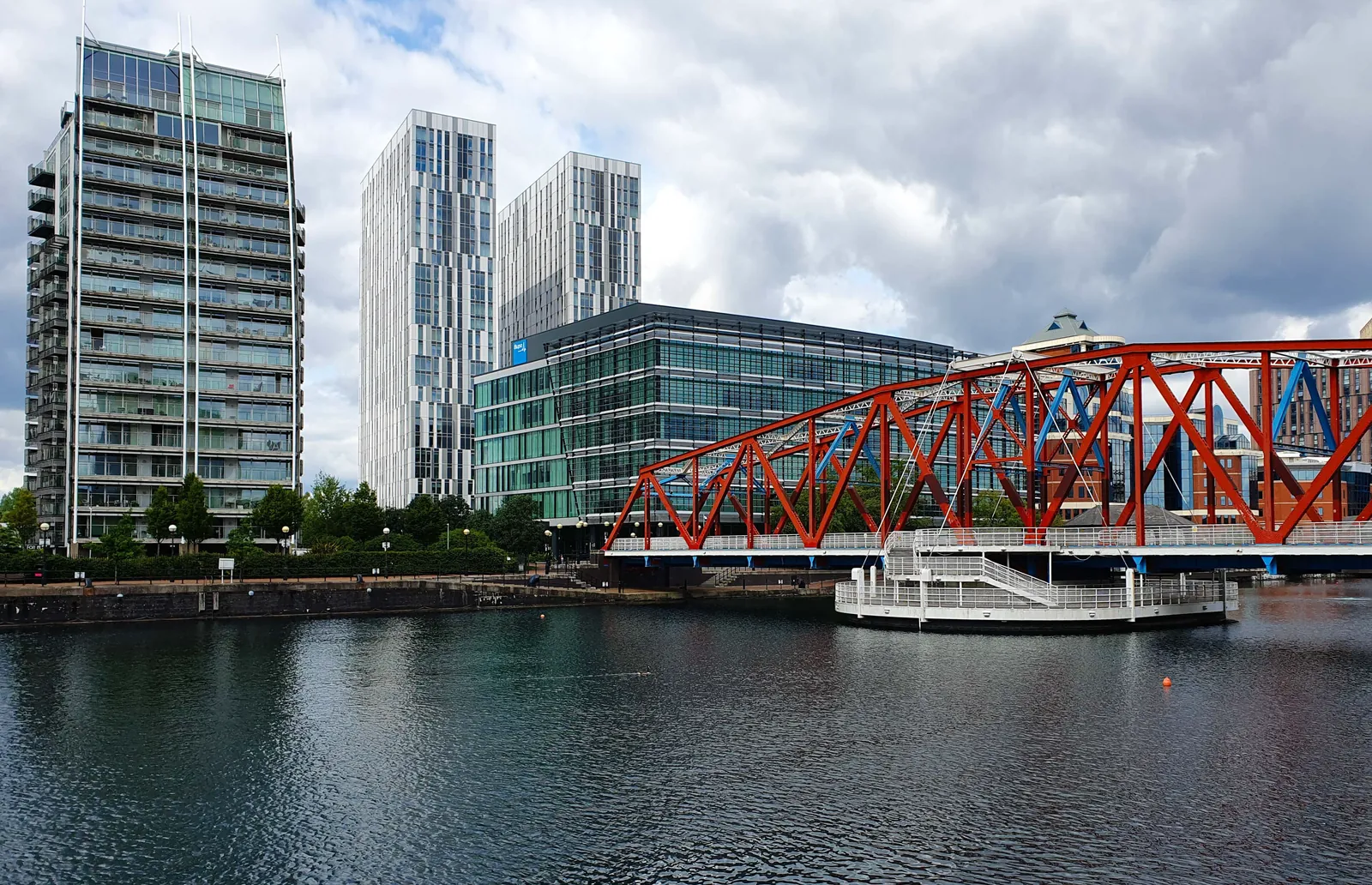 Tall glass towers and a red steel bridge over the water at Salford Quays